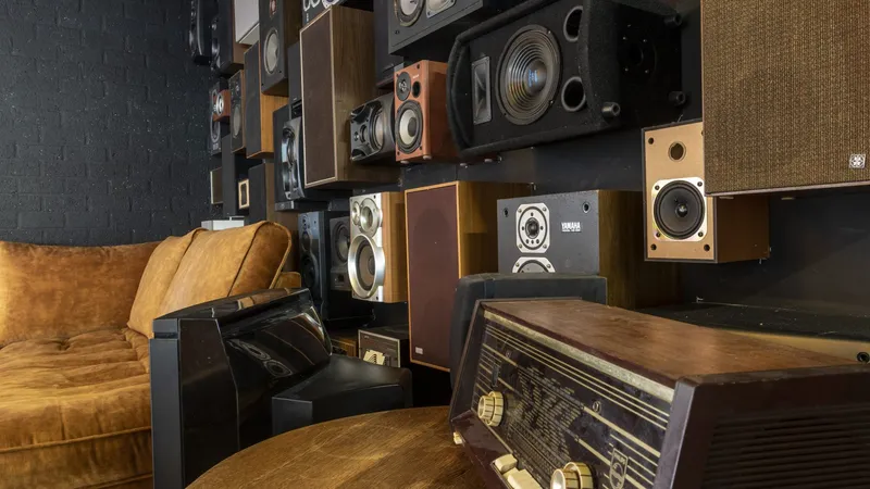 Een muur vol oude luidsprekers in de studio bij Bankastudios, met een bank en een ouderwetse radio ervoor