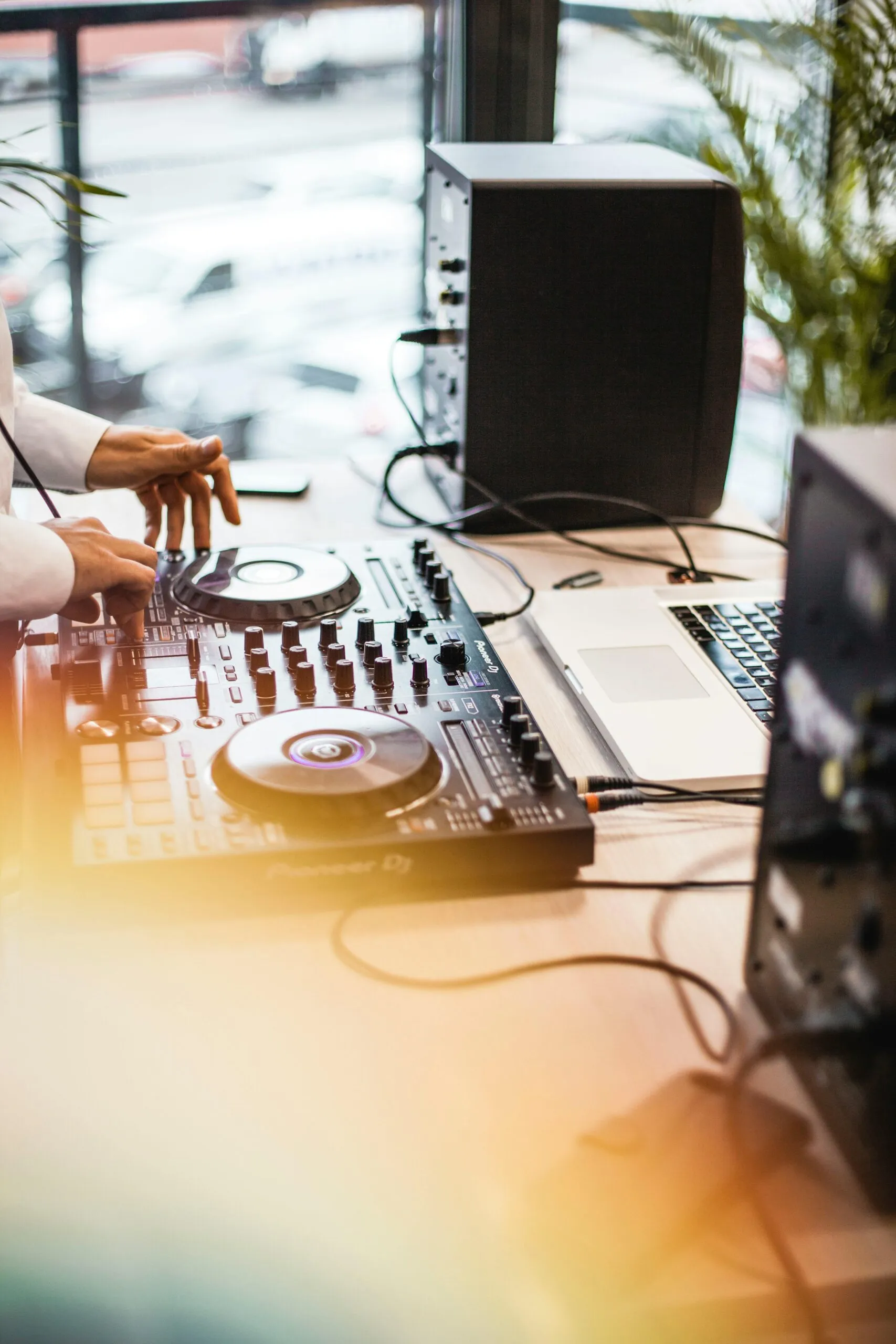 Handen van een DJ op een DJ-controller, met monitorspeakers en een laptop op tafel